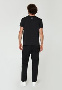 Sort atletisk t-shirt og bukser lavet af letvægtsstof med et enkelt design. Hvite sneakers fuldender outfittet.