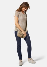 Beige gebreide top met een V-hals en korte mouwen; gecombineerd met donkerblauwe skinny jeans. Draagt een kleine beige crossbody tas; op de voeten lichte sneakers.