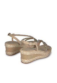 Beige wedge sandalen met een gevlochten touwplatform. Heeft een verstelbare band en een versierde bovenkant met heldere stenen. Zachte suède textuur.