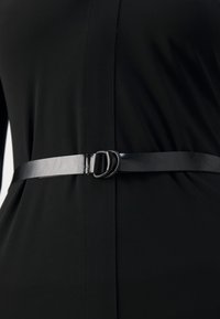 Gros plan d'une robe noire cintrée à la taille par une fine ceinture noire avec une boucle double anneau.