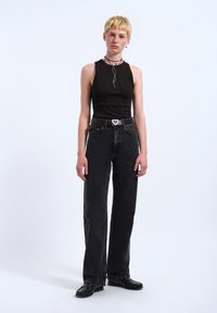 Black ribbed sleeveless top with a high neck, paired with high-waisted black wide-leg jeans and a black belt featuring a heart-shaped buckle.