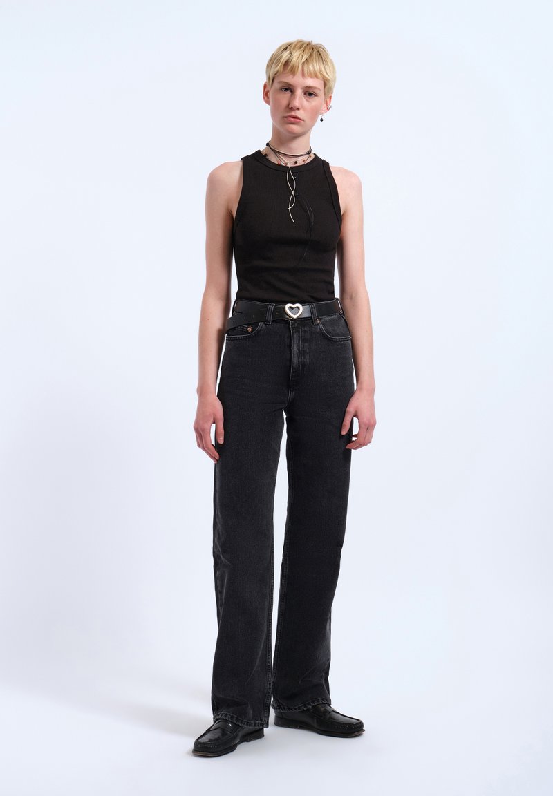 Black ribbed sleeveless top with a high neck, paired with high-waisted black wide-leg jeans and a black belt featuring a heart-shaped buckle.