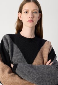 Suéter de malha com um design em blocos de cor em preto, cinza e bege; gola redonda; textura suave; ajuste oversized com padrões diagonais audaciosos.
