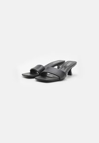 Mules noires en cuir à bout ouvert avec un bout carré, deux larges bandes sur le pied et un talon bloc de hauteur moyenne. Texture lisse et design minimal.