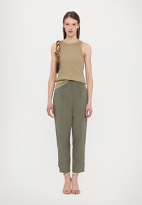 Khaki tank top paired with olive green tailored pants. The outfit features a relaxed fit and smooth texture. Strap with geometric accents.
