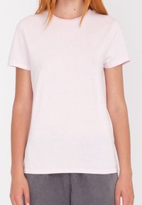 Vaaleanpunainen lyhythihainen T-paita pehmeästä kankaasta, jossa pyöreä kaulus ja pieni logokoriste rinnassa. Sileä pinta.