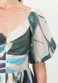 Blumenmusterkleid mit tiefem V-Ausschnitt, Puffärmeln und gerafftem Bund. Hergestellt aus leichtem, durchscheinendem Stoff in Blau-, Grün- und Rosatönen.