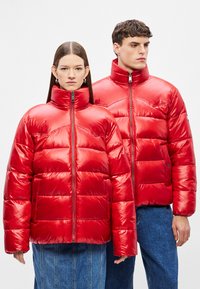 Κόκκινα μπουφάν τύπου puffer με γυαλιστερό φινίρισμα, που διαθέτουν ψηλό γιακά, κλείσιμο με φερμουάρ και ραμμένο σχέδιο. Κατάλληλα για άνδρες και γυναίκες.