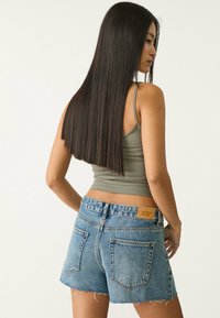Un débardeur gris ajusté associé à un short en denim bleu effiloché ; le short présente des détails en patch et un léger délavage, avec des poches arrière visibles.