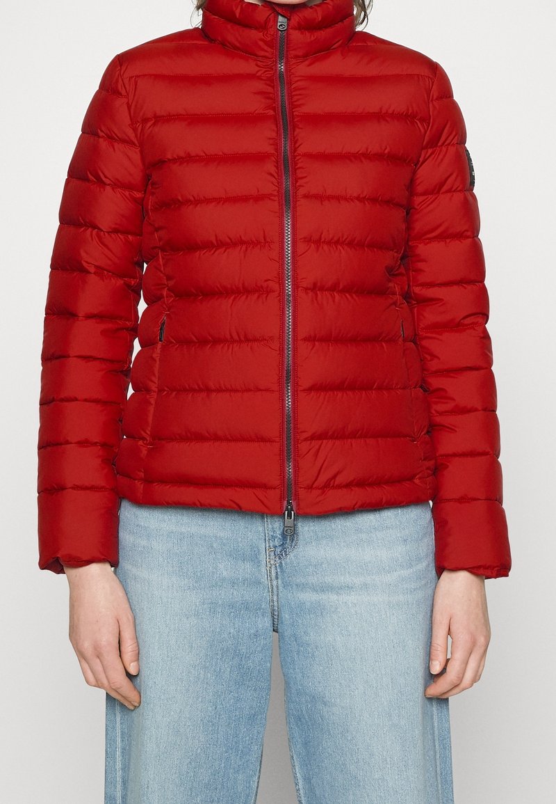 Červená prošívaná bunda s vodorovným prošíváním, vysokým límcem a předním zipem. Měkká látka s mírným leskem; obsahuje boční kapsy.