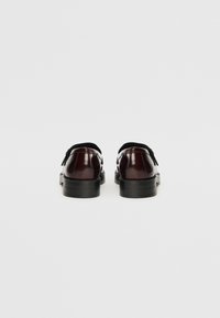 Burgundy leather shoes with a glossy finish, featuring a closed back and black rubber sole, accented with a decorative strap detail.