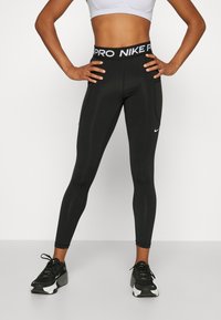 Mustat urheiluleggingsit, joissa on korkea vyötärö ja valkoiset "PRO NIKE" -brändäykset, silkinpehmeä materiaali, istuva malli ja sivutaskut.