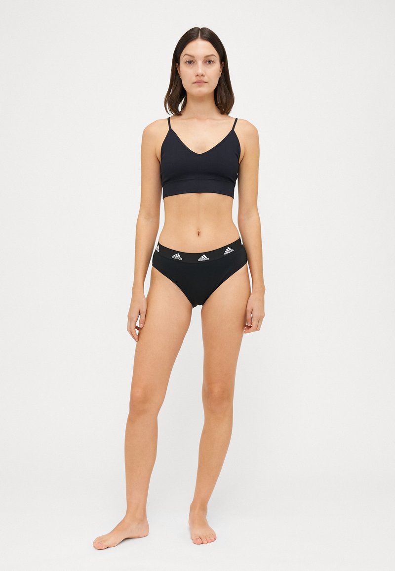 Melnā sporta krūšturis ar plānām siksnām, apvienots ar melnām augsto vidukļa biksītēm ar elastīgu jostu un baltā logotipa akcentiem.