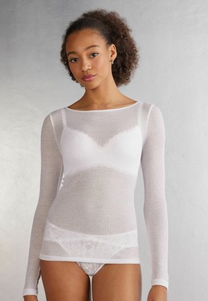 Witte lange mouw, geribbelde shirt met een scoop halslijn, gelaagd over een witte kanten beha en bijpassend kanten ondergoed. Zachte, doorschijnende textuur.