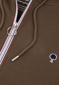 Felpa marrone con zip ad anello argentata, fodera a righe rosse e bianche, coulisse e piccolo logo di un albero ricamato sul petto.
