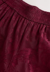Burgundy elastisk talje nederdel med et blødt, tekstureret stof og et subtilt bladmønster samt en svævende design.