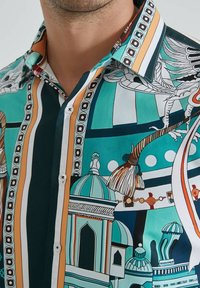 Gros plan sur la chemise d'un homme avec des motifs teal, orange, noir et blanc présentant des dômes architecturaux, des plumes et des bordures rayées.
