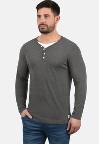 Langærmet grå henley-skjorte med v-hals og tre-knaps lukning; blød, strikket stof; parret med blå jeans.