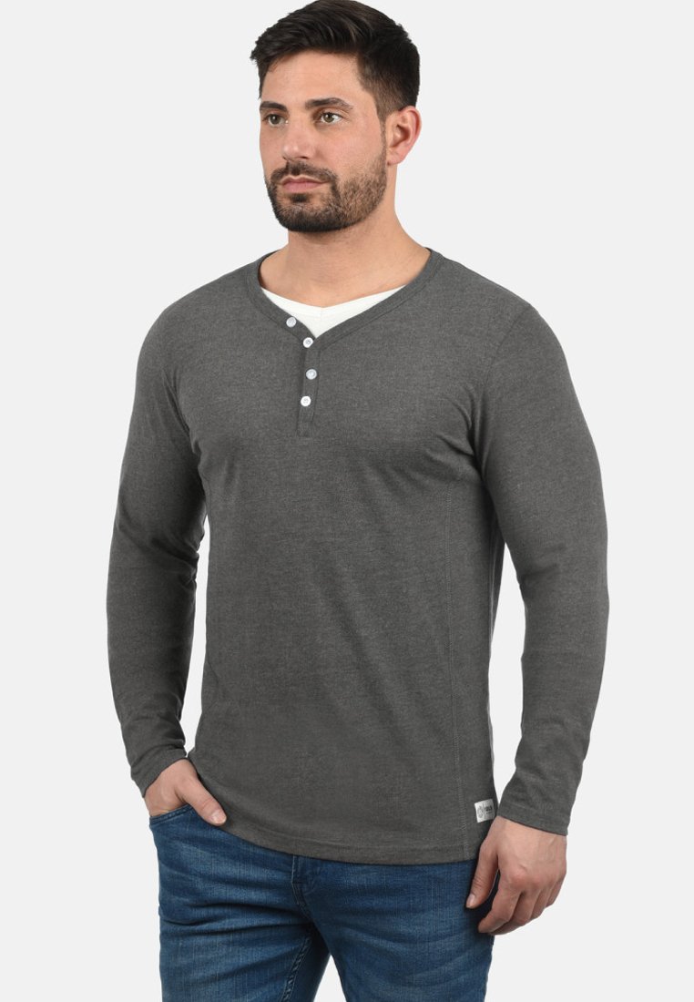 Langærmet grå henley-skjorte med v-hals og tre-knaps lukning; blød, strikket stof; parret med blå jeans.