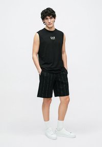 Must mustata kampsunit logoga, millele on lisatud mustad lühikesed püksid peene tekstitrükiga. Valged tossud ja sokid lõpetavad komplekti.