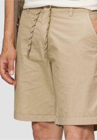 Shorts beiges avec une texture lisse, dotés d'une fermeture à cordon de serrage avec des accents noirs, de poches latérales et de ourlets retroussés.