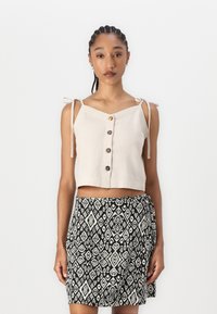 Sydd lett beige topp med tynne stropper og knappene foran, kombinert med et svart og hvitt mønstret omslagskjørt med diamantmotiver.