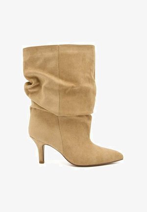 Botte souple en daim beige mi-mollet avec bout pointu et talon fin de hauteur moyenne, vue de côté sur fond blanc uni.