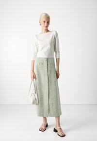 Hvit langermet topp, grønn tweed midi-skjørt med knapper, kombinert med svarte blokkhelte sandaler og en hvit håndveske. Enkelt design.