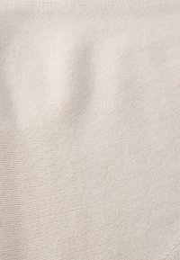 Gros plan sur un tissu beige tricoté avec une texture douce visible et des détails fins de points horizontaux.