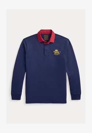 Μπλε ναυτικό πόλο με μακριά μανίκια, κόκκινο γιακά, κεντητό χρυσό λιοντάρι και κούμπωμα με τρία κουμπιά. Μαλακό βαμβακερό υλικό.
