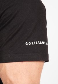 Černé bavlněné tričko s krátkými rukávy a bílým logem "GORILLAWEAR" na levém rukávu. Hladká textura, přiléhavý střih.