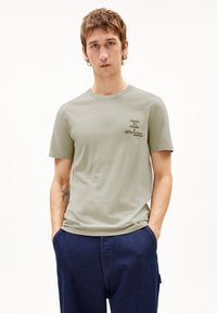 Lichtgroen katoenen t-shirt met korte mouwen, ronde hals, met zwarte tekst op de linkerborst die zegt "Gemaakt om een verschil te maken."