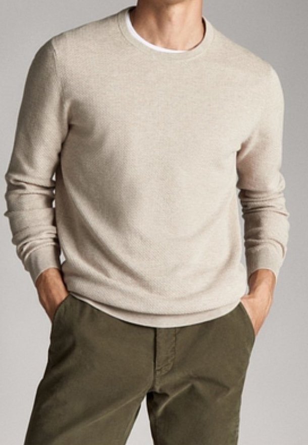 Beige stickad tröja med rund halsringning, långa ärmar och ett strukturerat mönster, parat med olivgröna byxor.