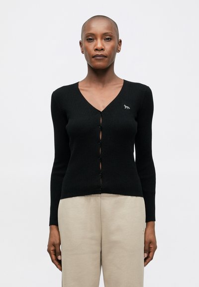 Cardigan noir côtelé avec un col en V et des manches longues, comportant une fermeture à bouton et un petit motif brodé sur la poitrine.