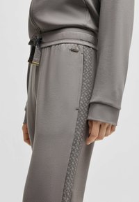 Gray sweatpants made of soft fabric feature a patterned side stripe, ribbed cuffs, and a drawstring waist. Subtle logo detail present.