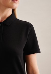 Czarna koszulka polo z teksturowanej tkaniny, klasycznym kołnierzykiem i krótkimi rękawami. Posiada zapięcie na trzy guziki oraz subtelne detale szycia.