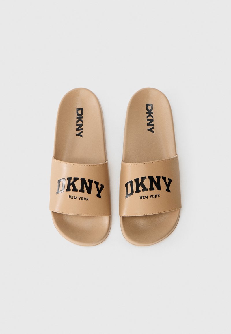Chanclas de color marrón hechas de un material sintético suave. Cuentan con una tira ancha con el texto negro "DKNY NEW YORK". Tienen una forma redondeada y un diseño minimalista.