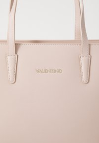 Rozā teksturēta soma ar divām rokturēm, priekšpusē centrā ir zelta "VALENTINO" logo. Gluda materiāla virsma ar maigiem šuvju elementiem.