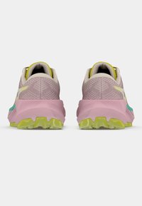 Ténis de corrida leves em rosa e bege com parte superior texturada, detalhes verdes, solas grossas cor de rosa e tacos de tração multidirecionais.