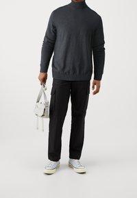 Pull à col roulé gris foncé, pantalon cargo noir, baskets bleu clair, et un petit sac bandoulière blanc avec des bretelles grises.