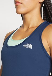 Navy blue athletic tank top with a mint green inner layer, featuring The North Face logo. Smooth, fitted texture and classic sleeveless design.