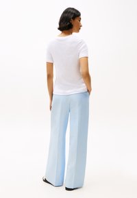 Un tricou alb cu mânecă scurtă, asortat cu pantaloni largi de culoare albastră deschisă, ambele având o textură netedă. Sandale vizibile pe picioare.