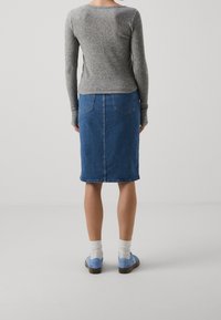 Graues, rippiertes Langarmoberteil mit rundem Halsausschnitt, kombiniert mit einem Jeans-Bleistiftrock. Blaue Schuhe und weiße Socken vervollständigen das Outfit.