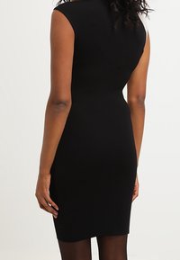 Abito nero aderente con design senza maniche, tessuto testurizzato e silhouette sinuosa, caratterizzato da un taglio al ginocchio e dettagli posteriori.