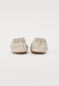 Beige stoffstoffslippers med blomstermønster, samlet ankeldesign, flate såler og lett avrundet tåform. Myk tekstur, lett.