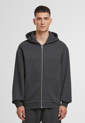Sivá mikina na zips vyrobená z mäkkej tkaniny, s veľkou kapucňou, prednými vreckami a rebrovanými manžetami. Jednoduchý dizajn s voľným strihom.