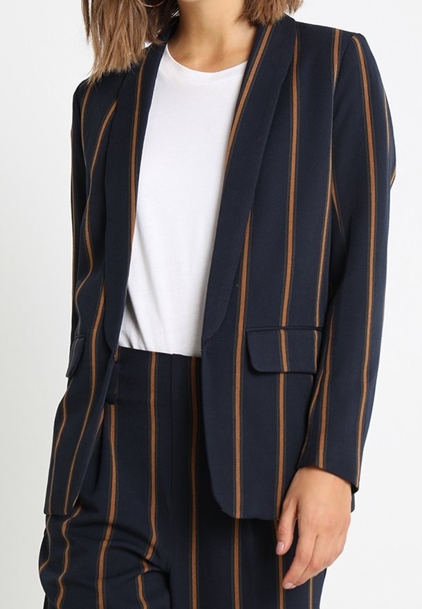 Granatowa marynarka w brązowe pionowe paski, dopasowany krój, zapięcie na jeden guzik i dwie przednie kieszenie, noszona na białym t-shircie.