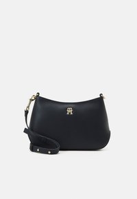 Borsa a tracolla in pelle nera con forma curvata, hardware dorato, tracolla regolabile e accentuazione del logo frontale. Texture liscia, design minimale.