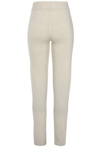 Beige legging gemaakt van een zachte, gestructureerde stof. Ze hebben een geribde tailleband en een getailleerd ontwerp dat smal toeloopt bij de enkels.