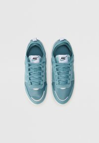 Sneakers Nike azul claro com parte superior em malha e sintético, bico redondo, atacadores planos e sola de borracha branca. Apresenta detalhe do logotipo na língua.